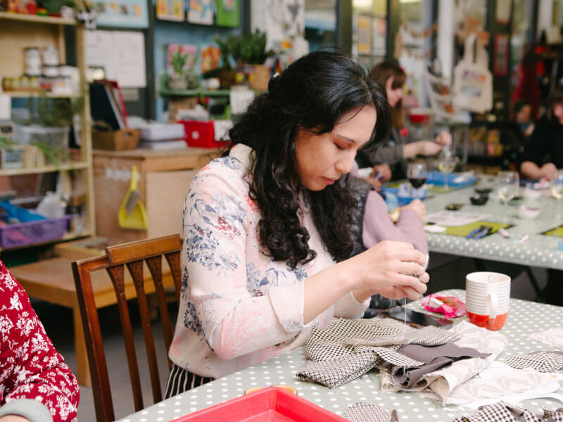 Woman surrounded by fabric, concentrating on sewing something